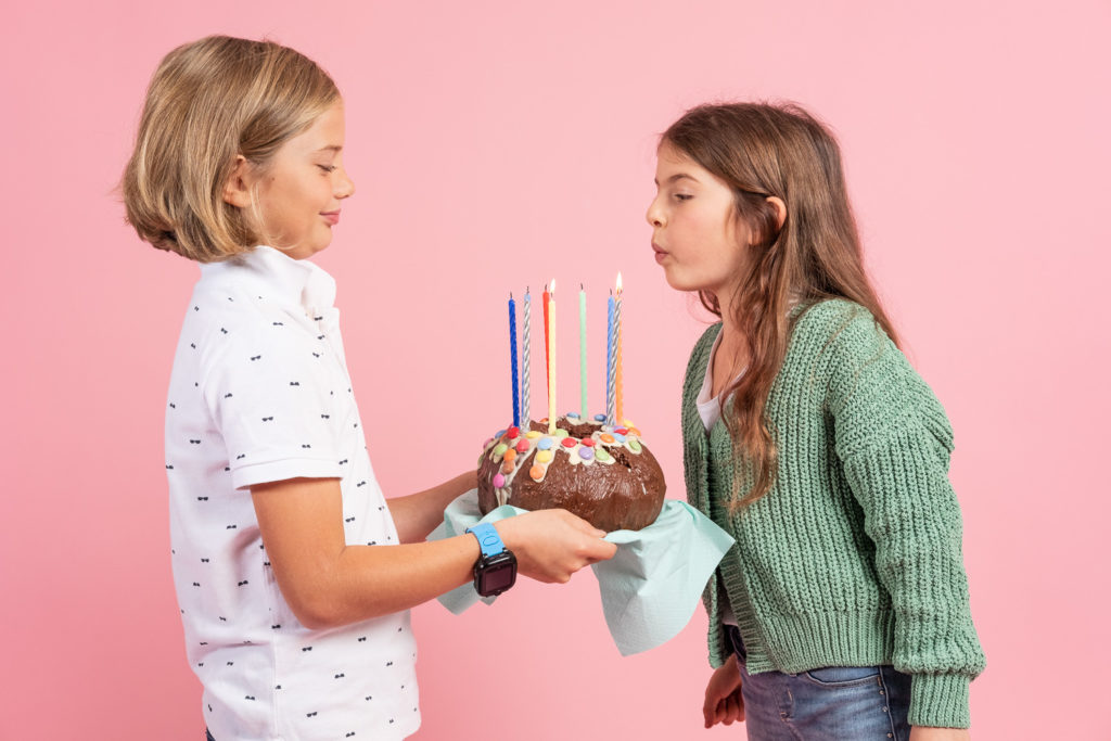 Barnkalas, bar står och blåser ut en tårta, rosa bakgrund. 